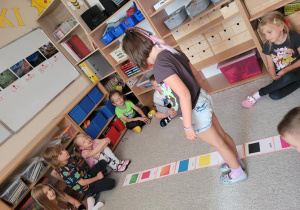 Dzieci skaczą obok obrazków rozłożonych na dywanie i nazywają właściwy kolor po angielsku.