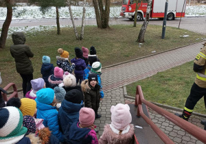 Dzieci idą na miejsce zbiórki, w oddali widać parkujący wóz strażacki