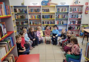 Dzieci siedzą na kolorowych krzesełkach w półkolu na tle ksiązek