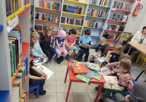 Dzieci siedzą na kolorowych krzesełkach w półkolu i oglądają ksiązki