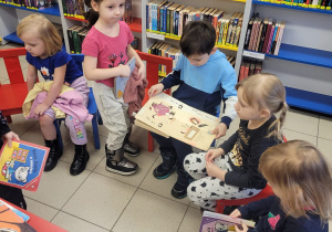 Dzieci siedzą na kolorowych krzesełkach w półkolu i oglądają książki