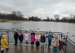 Dzieci stoją na tle pływających kaczek po Stawach Jana