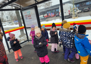 Dzieci stoją na przystanku, czekają na autobus, jedzą słodkości