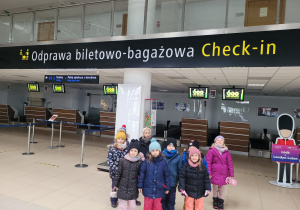 Dzieci pozują przed działem ,, Odprawa biletowo- bagażowa'' na lotnisku