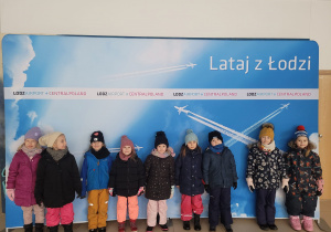Dzieci pozują przy tablicy na lotnisku ,, Lataj z Łodzi''