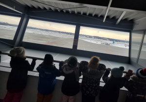 Dzieci oglądają jak wygladą płyta lotniska i samolot tam stojący