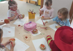 Dzieci przy stolikach malują farbami pączki