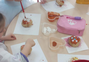 Dzieci przy stolikach malują farbami pączki