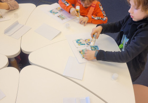 Dzieci przy stolikach układają historyjkę obrazkową o smoku wawelskim