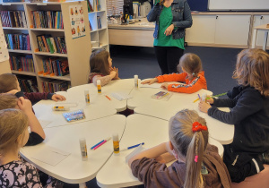 Pani z biblioteki prezentuje prace -smoka wawelskiego, którego wykonają dzieci. Dzieci grzecznie siedzą przy stolikach