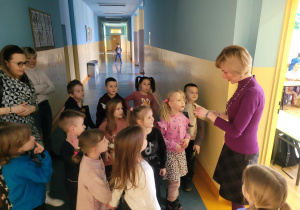 Dzieci stoją przed drzwiami klasy, wita ich nauczycielka Pani Sylwia