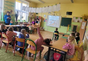 Dzieci siedzą w ławce szkolnej i oglądają prezentacje o różnego rodzaju pisankach