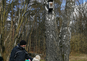 Dzieci słuchają przewodnika i stoją wokół drzewa