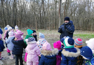 Dzieci słuchają przewodnika który opowiada o ciekawostkach lasu