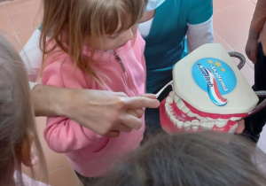 Zosia przy pomocy Pani Stomatolog myje zęby na specjalnej dentystycznej jamie ustnej