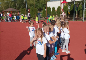 Dzieci stoją na boisku ubrani na sportowo. Jagódka macha do aparatu