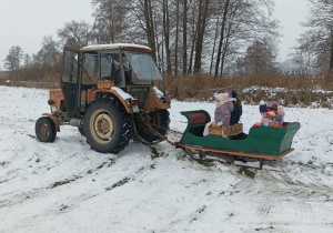 Dzieci siedzą w saniach , mają przejazdzke