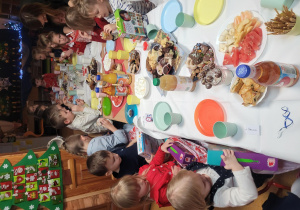 Dzieci siedzą przy zastawionymi stołami, ogladają otrzymane prezenty