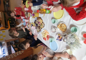 Dzieci siedzą przy zastawionymi stołami, jedzą smakowitości