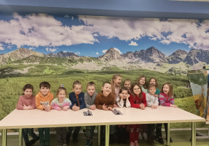 Dzieci pozują za stołem na tle fototapety w sali geograficznej