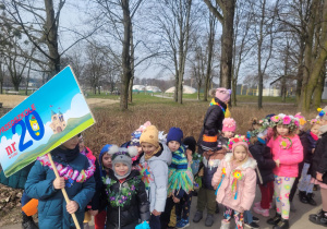 Dzieci w parach z transparentem z logo przedszkola stoją