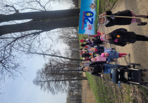 Dzieci i Julka z transparentem loga przedszkola idą w korowodzie wiosennym