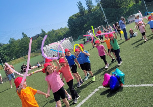 Dzieci z kolorowymi balonami idą boiskiem, prezentują się