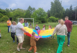 Dzieci wraz z rodzicami stoją przy kolorowej chuscie