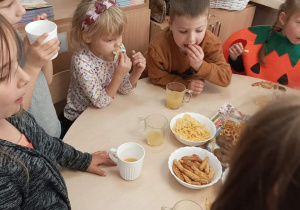 Dzieci jedzą przy stolikach słodkości.