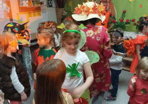 Dzieci tańczą w strojach- pani Jesieni, z nimi tańczy nauczycielka w kapeluszu pełnym liści.