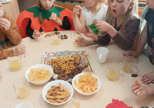 Dzieci siedzą przy stolikach i jedzą ciasta, paluszki.