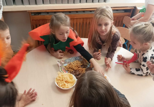 Dzieci jedzą przy stolikach ciasta, chipsy.