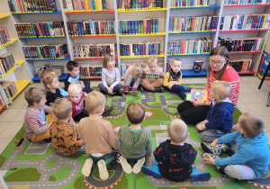 Dzieci siedzą na dywanie w bibliotece- wita ich Pani bibliotekarka