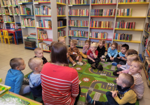 Dzieci siedzą na dywanie w bibliotece - rozmawiają z panią bibliotekarką