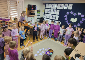 Dzieci stoją w kole, podają sobie fioletowy balon w rytm grany na gitarze