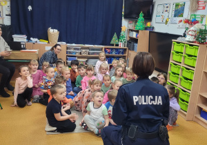 Dzieci siedzą na dywanie słuchają policjantki