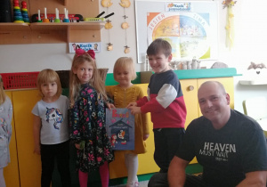 Dzieci wraz z tatą Szymka prezentują czytaną książkę i pozują do zdjęcia.