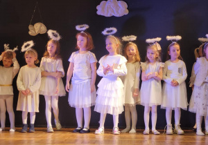 Dzieci w strojach aniołków i śnieżynek stoją na scenie