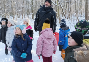Dzieci stoją i słuchają przewodnika na śniegu w lesie