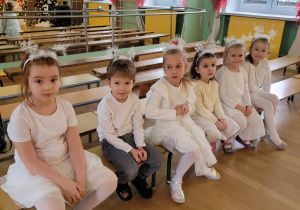 Dzieci ubrane na biało siedzą na ławce czekają na występ