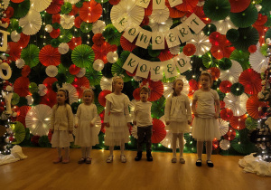 Dzieci śpiewają piosenkę, stoją na tle dekoracji