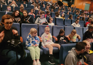 Dzieci siedzą na widowni i czekają na spektakl