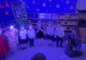 Maluchy stoją w półkolu śpiewają piosenkę przy akompaniamencie gitary