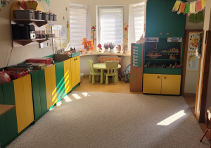 Klasa grupy Motylków. W klasie znajdują się zielono-żółte szafki, dywan w kolorze szarym. Pod oknem stoi mały okrągły stolik.
