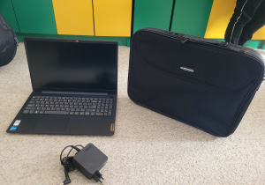 laptop z torba i ładowarką stoi na dywanie