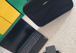 laptop z torba i ładowarką stoi na dywanie
